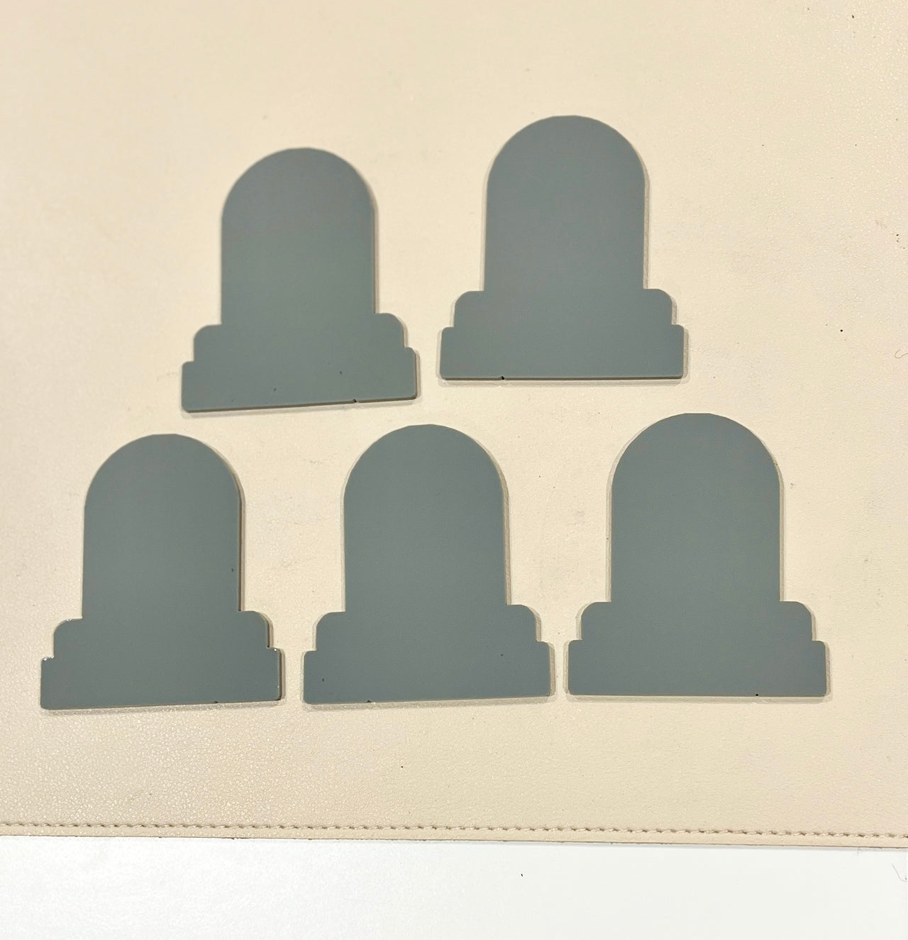 Five smooth-edged gray mirrored pieces with rounded tops arranged on a pale beige surface