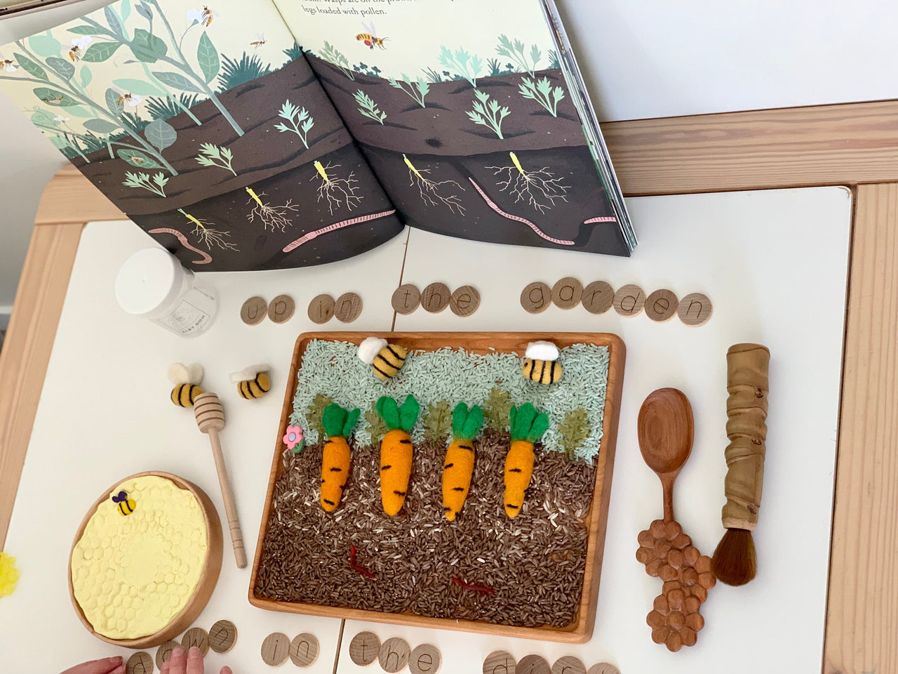 Large rectangular writing tray with felt carrots, wooden bees, honeycomb toy, wooden tokens, and open nature book on table