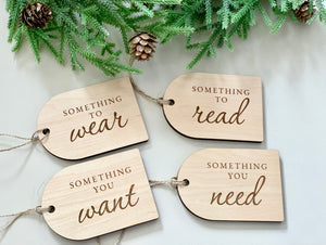 Set of four wooden Christmas gift tags engraved with phrases something you want, need, to read, to wear with pine and pinecones above