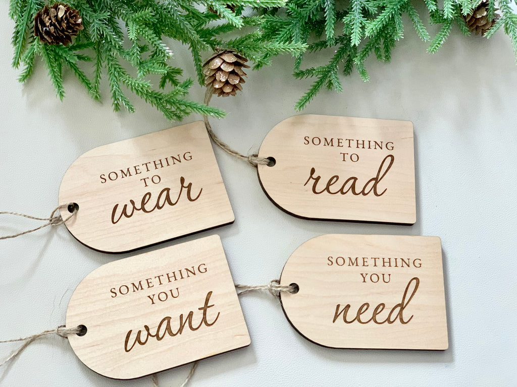 Set of four wooden Christmas gift tags engraved with phrases something you want, need, to read, to wear with pine and pinecones above