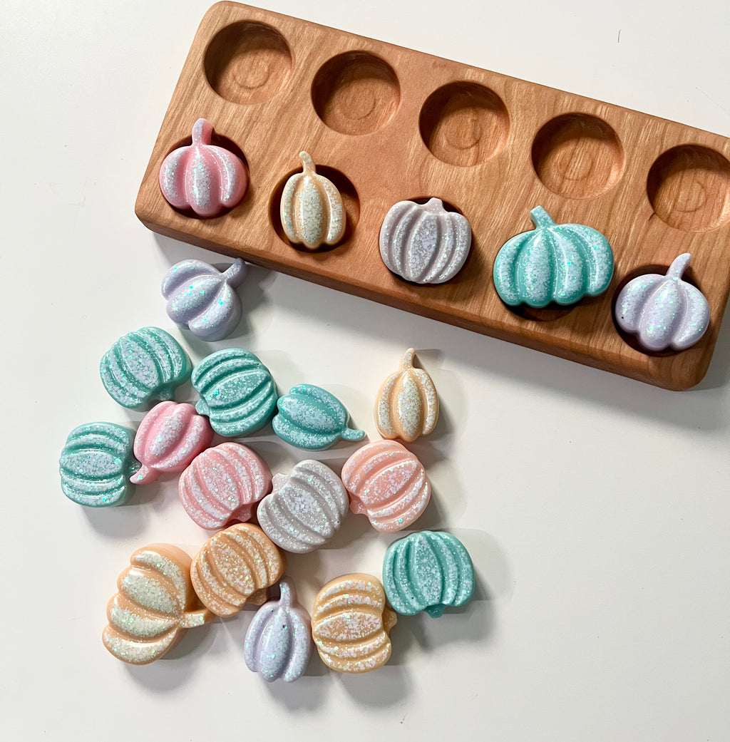 Orange pumpkin-shaped resin toys on a white surface with a wooden ten frame