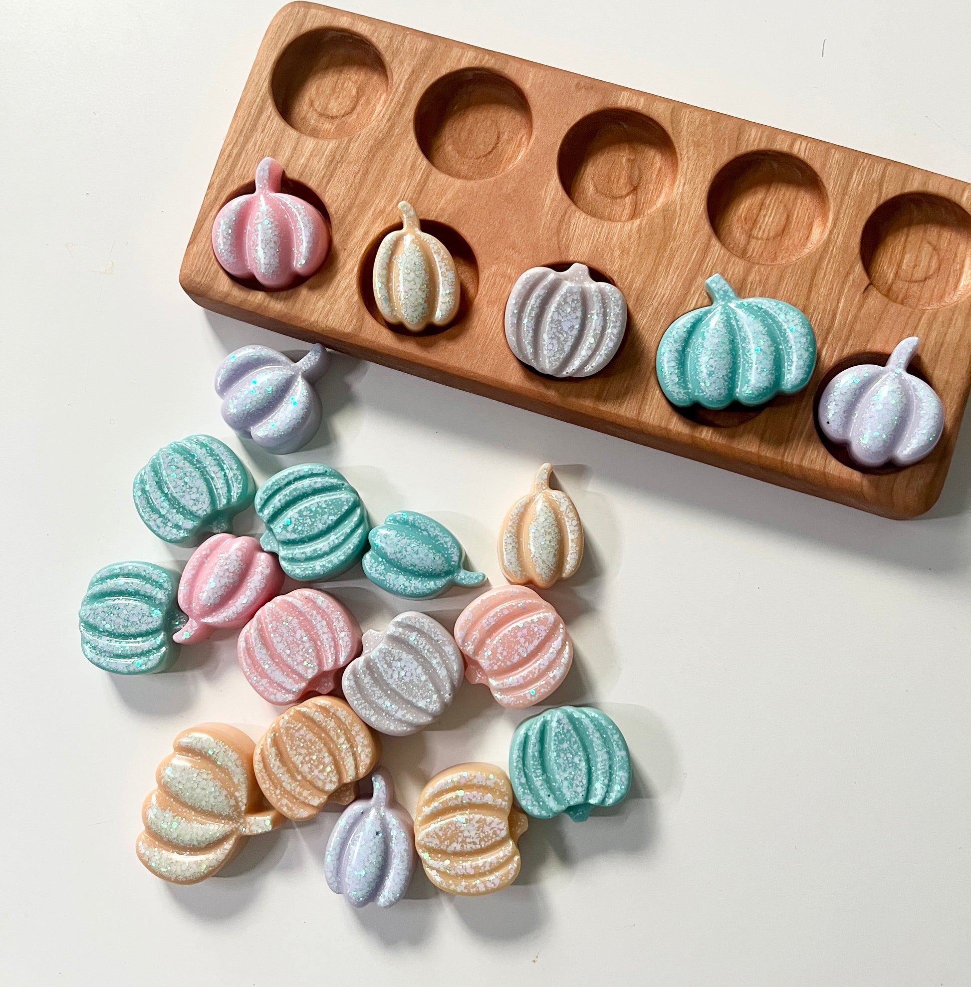 Orange pumpkin-shaped resin toys on a white surface with a wooden ten frame