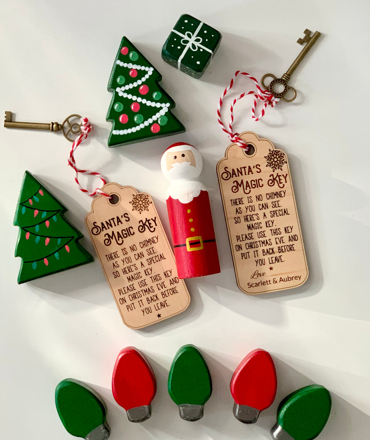 Wooden Santa’s Magic Key tags with red and white twine, wooden keys, Christmas trees, Santa figure, and light bulb ornaments on white surface