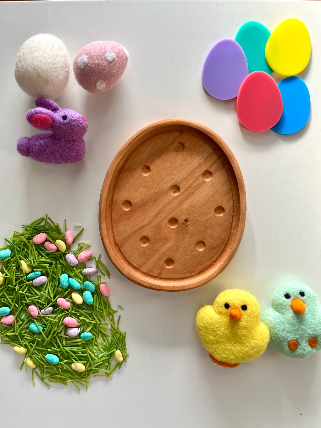 Oval wooden tray with colorful felt eggs, green pasta grass with pastel candy eggs, and felt bunny and chick figures nearby