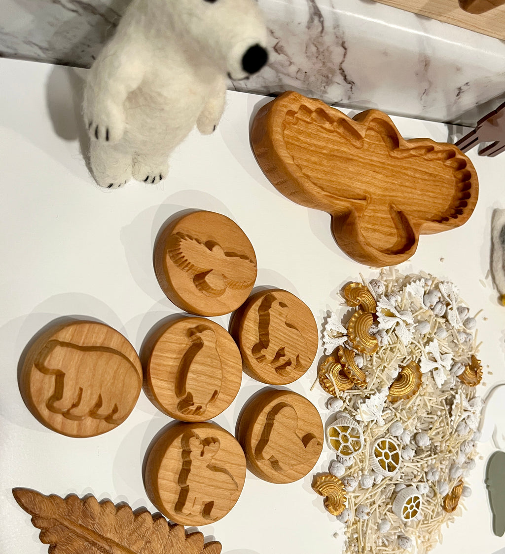 Wooden animal-shaped discs with engraved silhouettes, wooden moose tray, felt polar bear, and natural sensory materials on white surface
