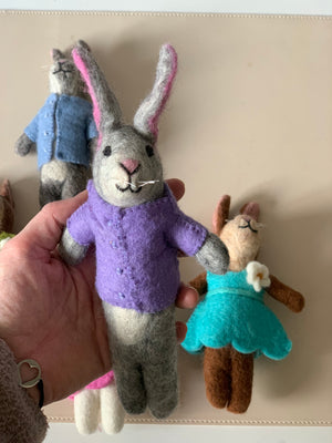 Hand-stitched gray felt bunny doll in a purple shirt held in hand with brown and gray bunnies in colorful clothes behind