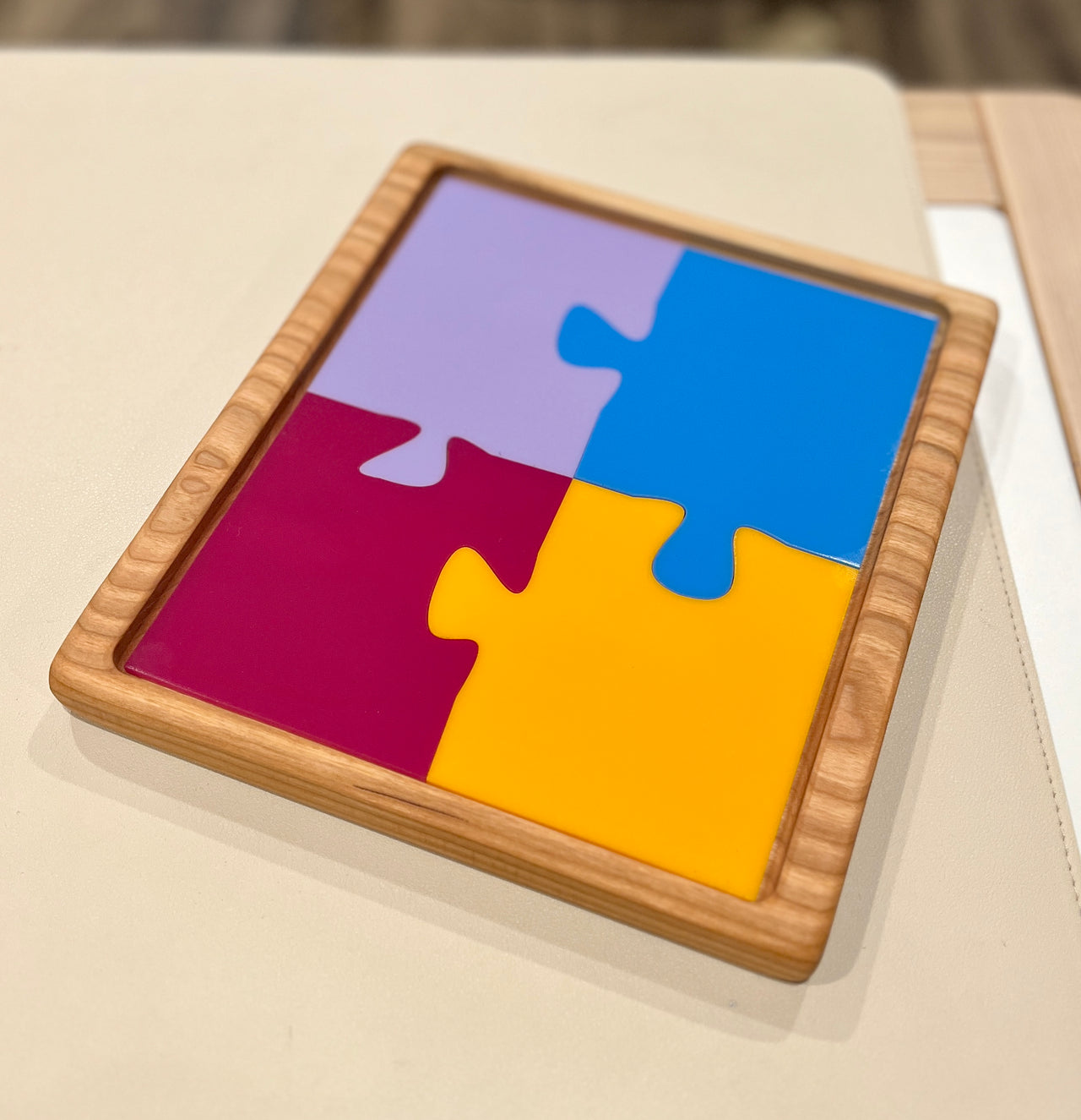Wooden tray holding four large colorful interlocking puzzle pieces in purple, blue, red, and yellow on a light surface