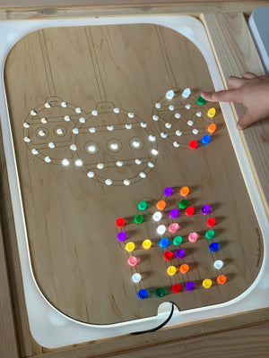Light wooden insert with Christmas ball and gift designs lit up by colorful pegs on Flisat large bin tabletop