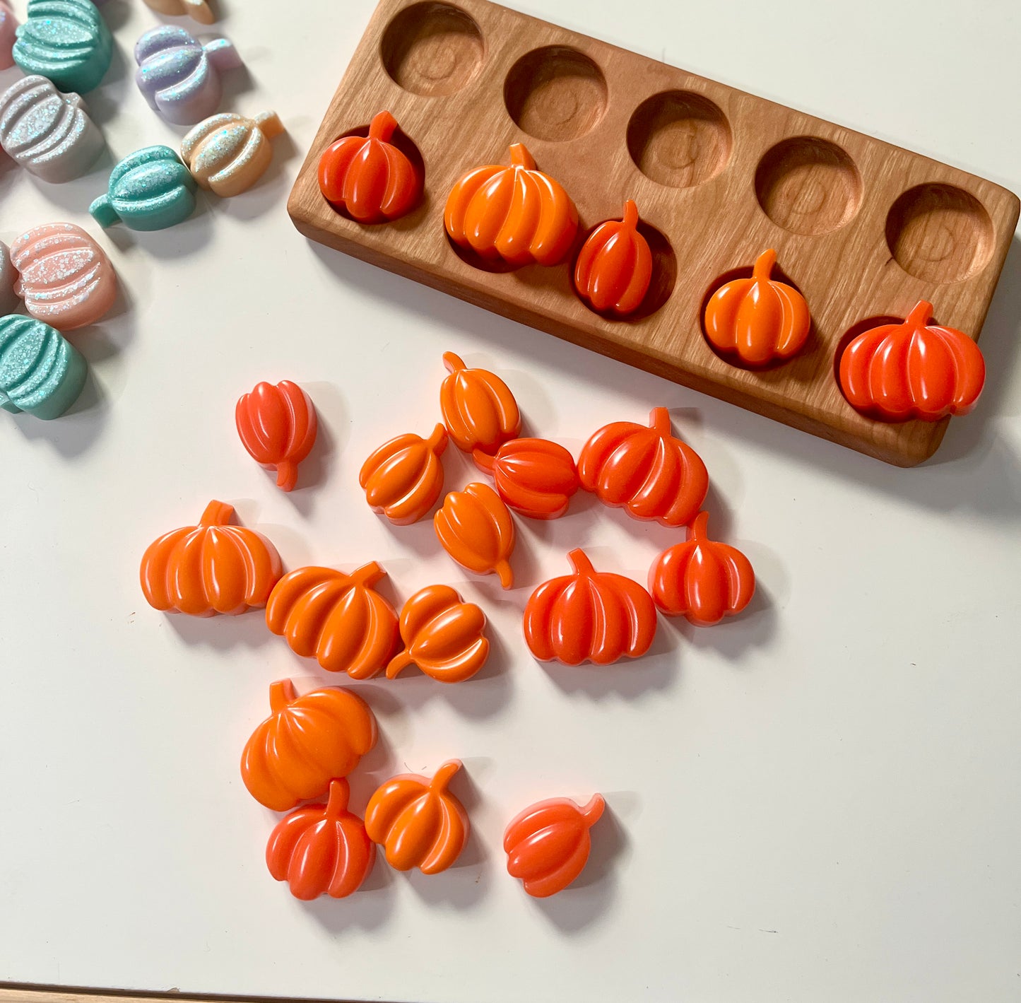 Orange pumpkin-shaped resin toys on a white surface with a wooden ten frame