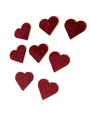 Eight red glitter-covered heart-shaped cutouts scattered on a plain white background