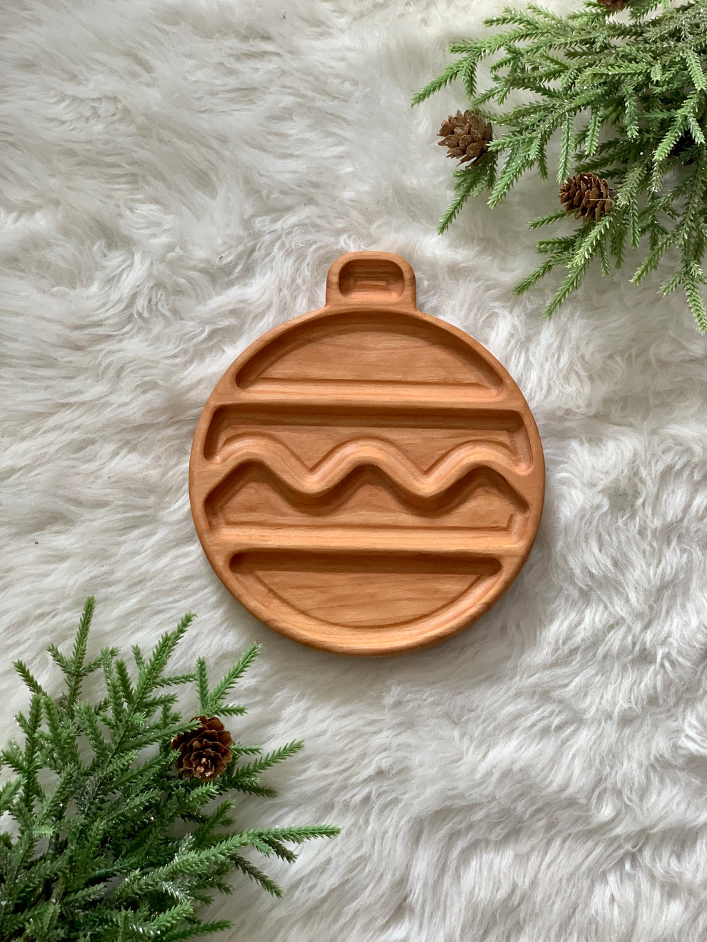 Ornament-shaped wooden sensory plate with carved wavy and straight grooves on white faux fur background with pine branches
