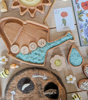Natural wooden segmented tray shaped like a watering can with green rice and wooden letter discs spelling GROW on wood table
