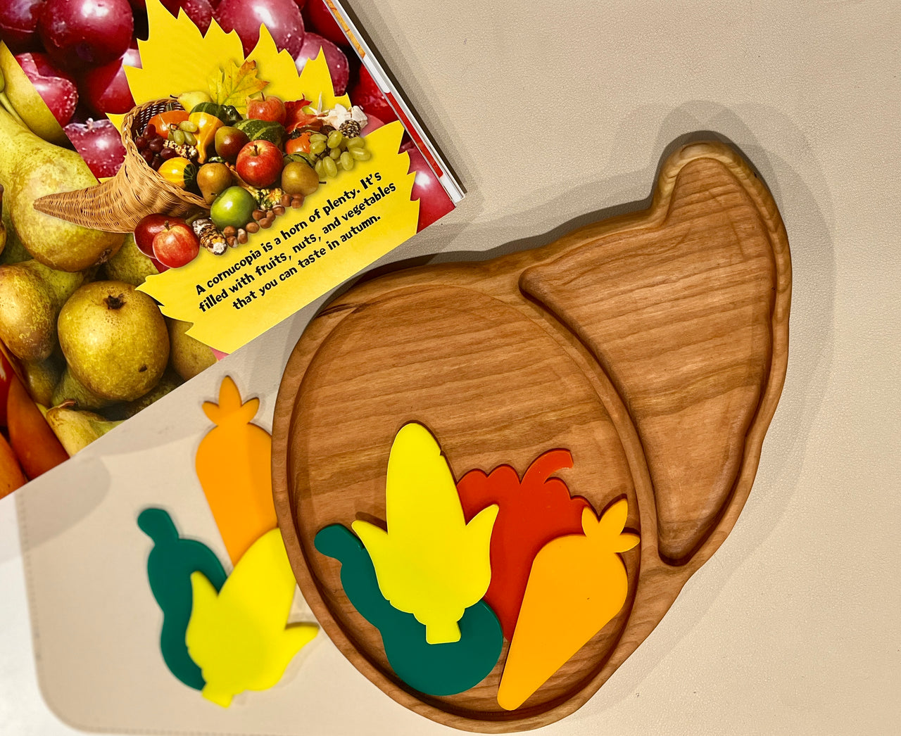 Smooth wooden tray shaped like a cornucopia with colorful foam fruits and vegetables on a beige surface