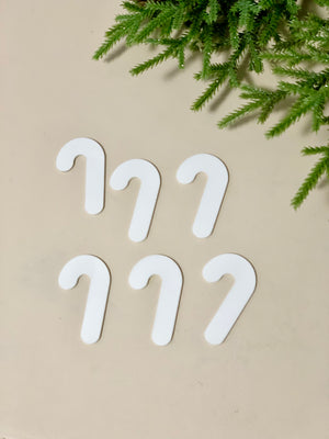 Set of six white candy cane-shaped dry erase boards arranged on beige surface with green pine branches above