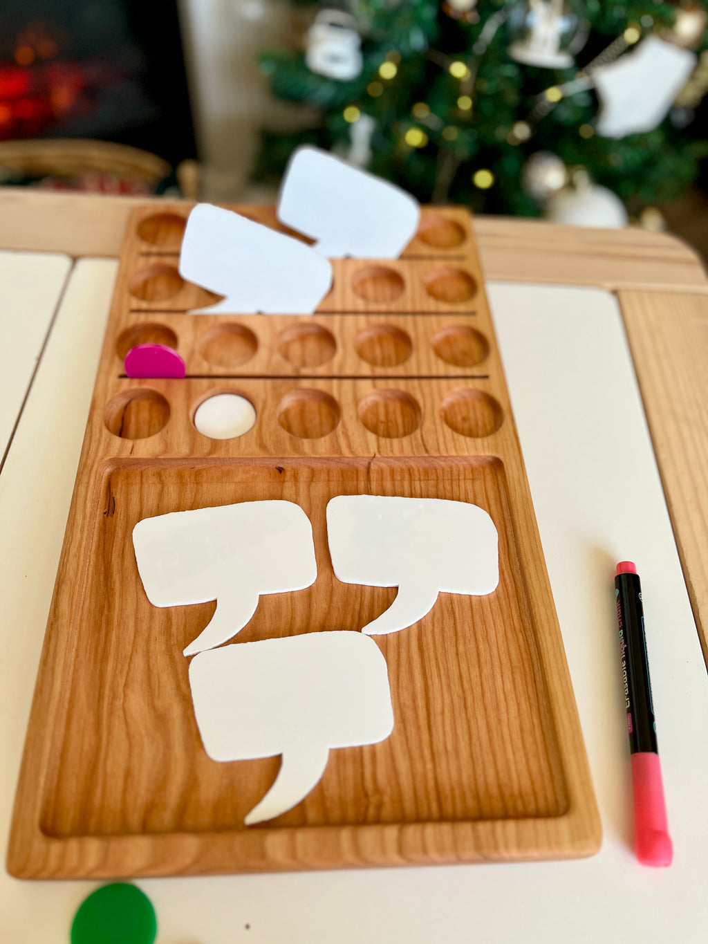 Wooden organizer tray with circular slots and blank white speech bubble cards alongside a pink marker on white table