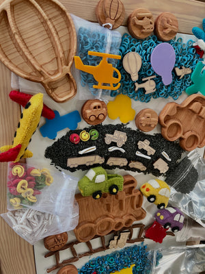 Wooden and felt vehicle-themed trays, stamps, and colorful rice pieces arranged on wooden surface with toy vehicles.