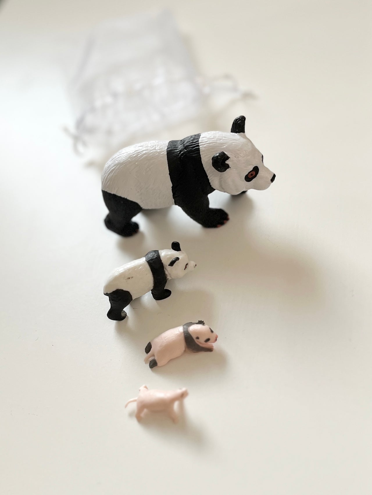 Four small animal figurines including two pandas and two pigs arranged on a white surface with a translucent pouch in the background