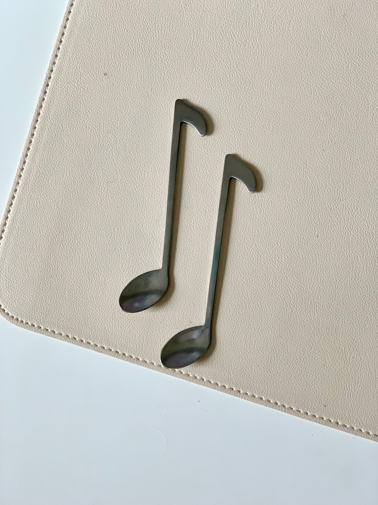 Pair of black metal spoons shaped like musical notes placed on a beige textured surface with stitching detail