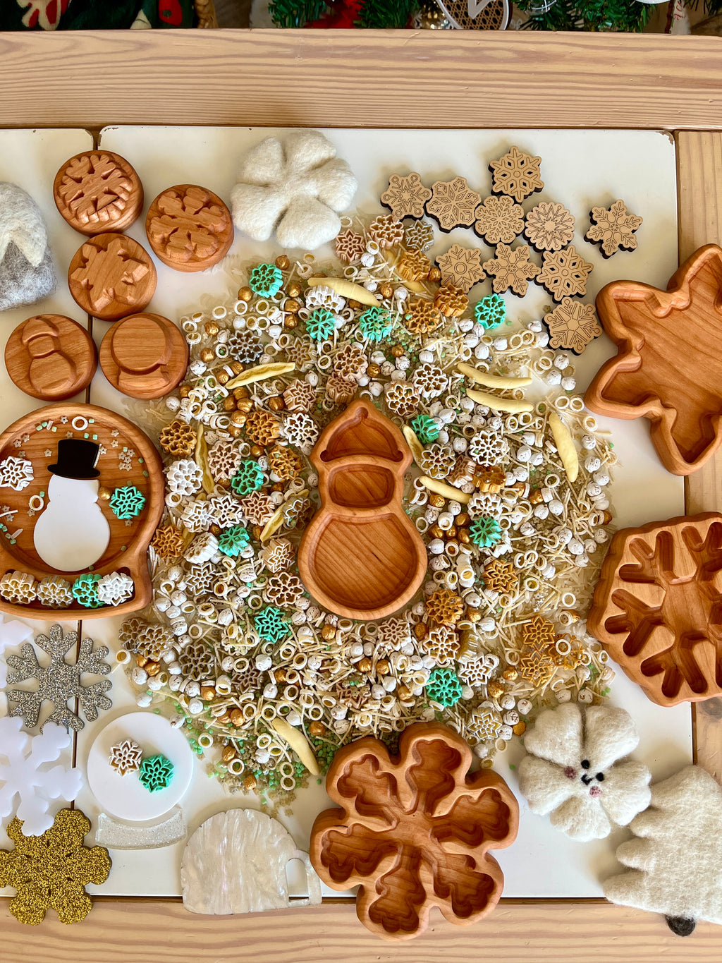 Wooden winter-themed trays and felt decorations arranged around a central pile of mixed beads and snowflake-shaped pieces