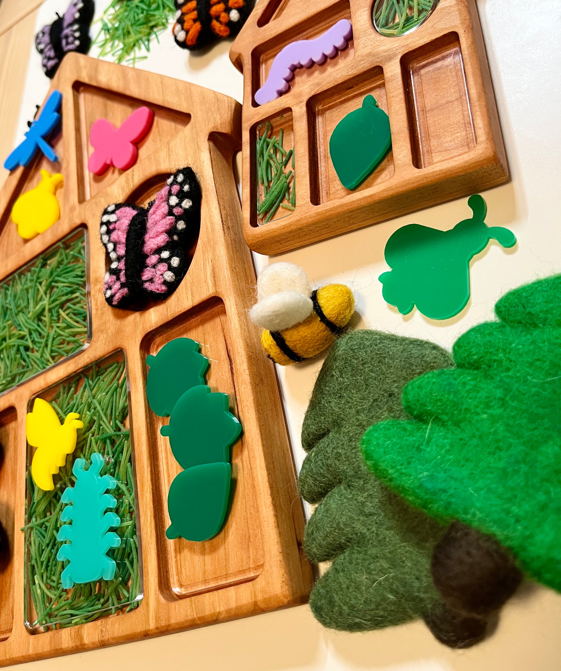 Wooden house shaped tray with compartments, with nature-themed felt and acrylic pieces including leaves, butterflies, and a bee on a light background.