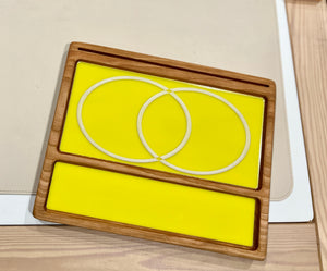 Smaller wooden multipurpose sensory tray with bright yellow dry erase inserts and overlapping circle outlines on wood surface