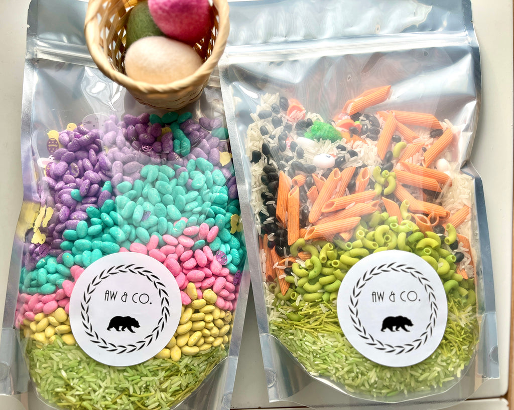 Two clear resealable bags filled with colorful dried beans, pasta, rice, and decorative felt balls in a small basket