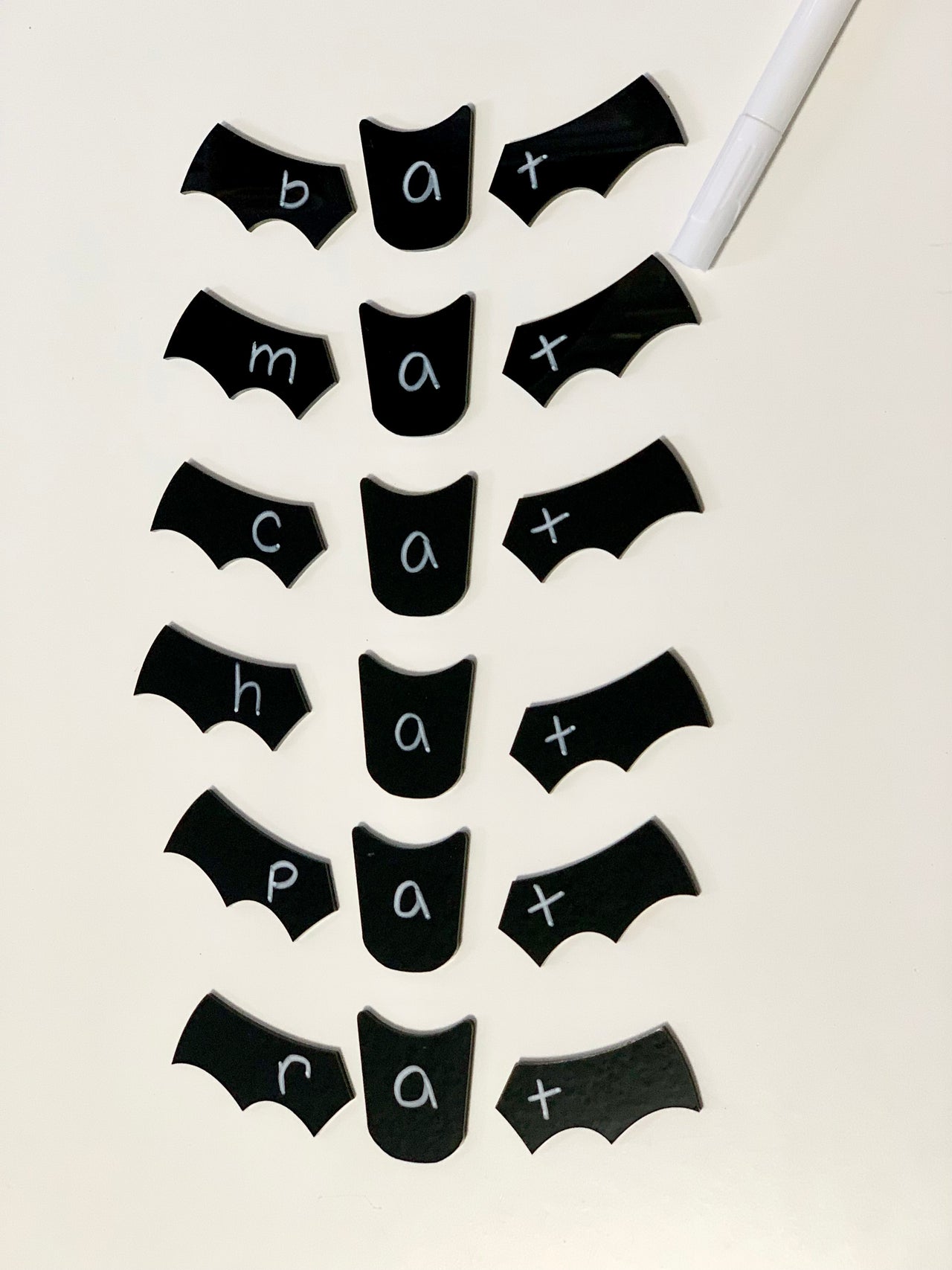 Black bat wing and center-shaped chalkboard labels with white handwritten words bat, mat, cat, hat, pat, rat on white surface