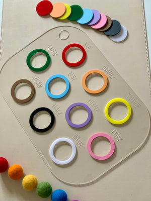 Clear rectangular colour sorting Flisat table bin lid with twelve coloured rings and matching felt balls on beige background