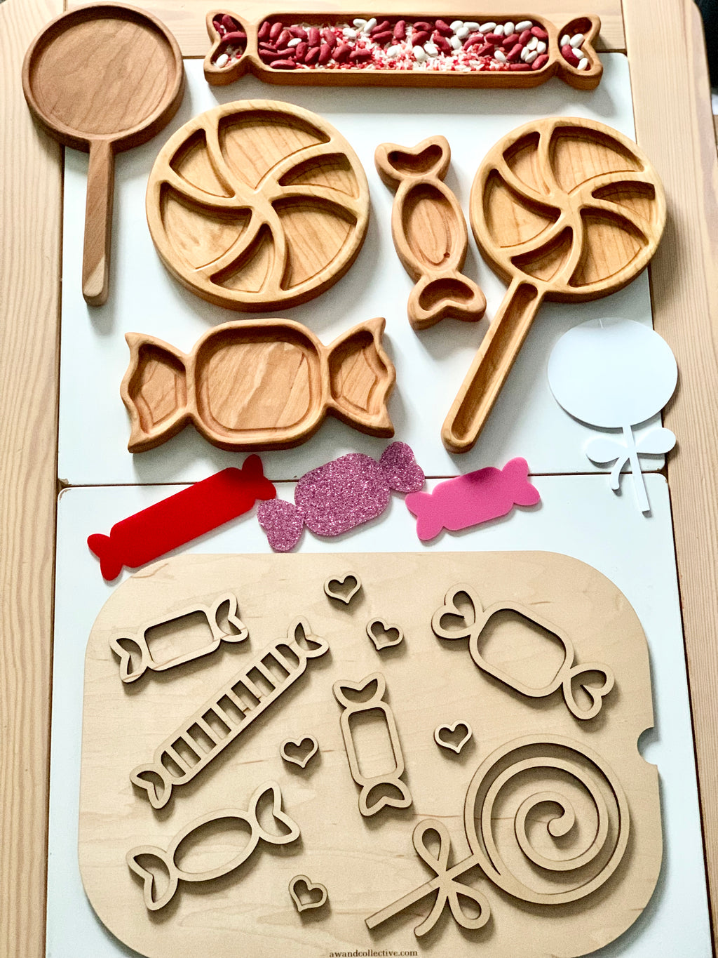 Wooden trays and puzzle pieces shaped like candies and lollipops with red and white beans and colorful paper cutouts on white surface