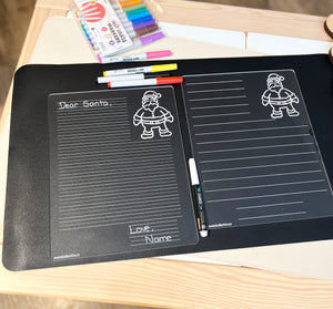 Clear acrylic writable board with lined sections and Santa Claus illustration, set on black surface with colorful markers nearby