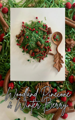 Leaf-shaped wooden spoon and a pile of green pine needle-like pieces with red berries and brown pinecone shapes on white background