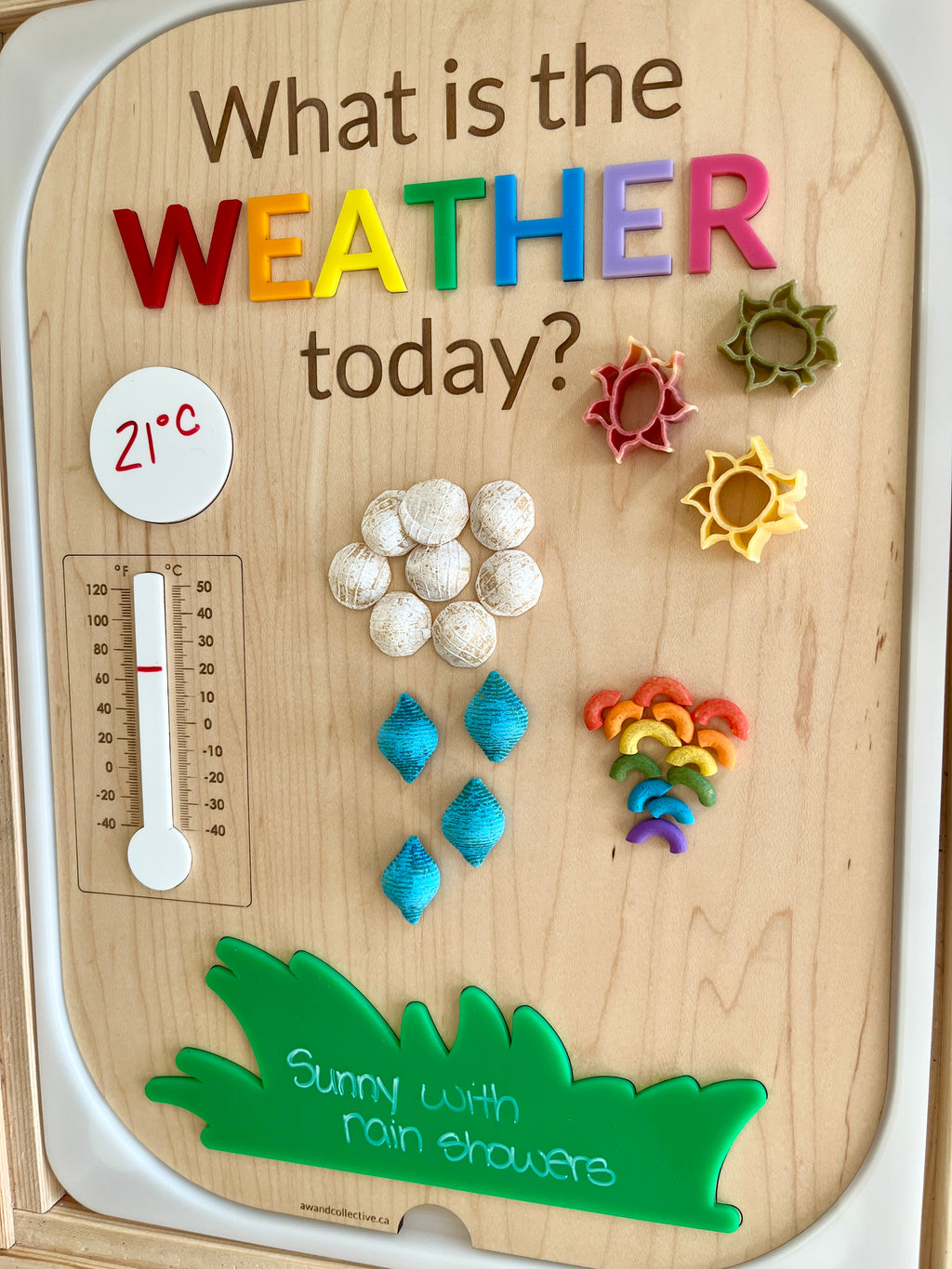 Wooden weather chart with colorful letters, magnetic pasta shapes for sun, clouds, rain, rainbow, and 21°C thermometer reading