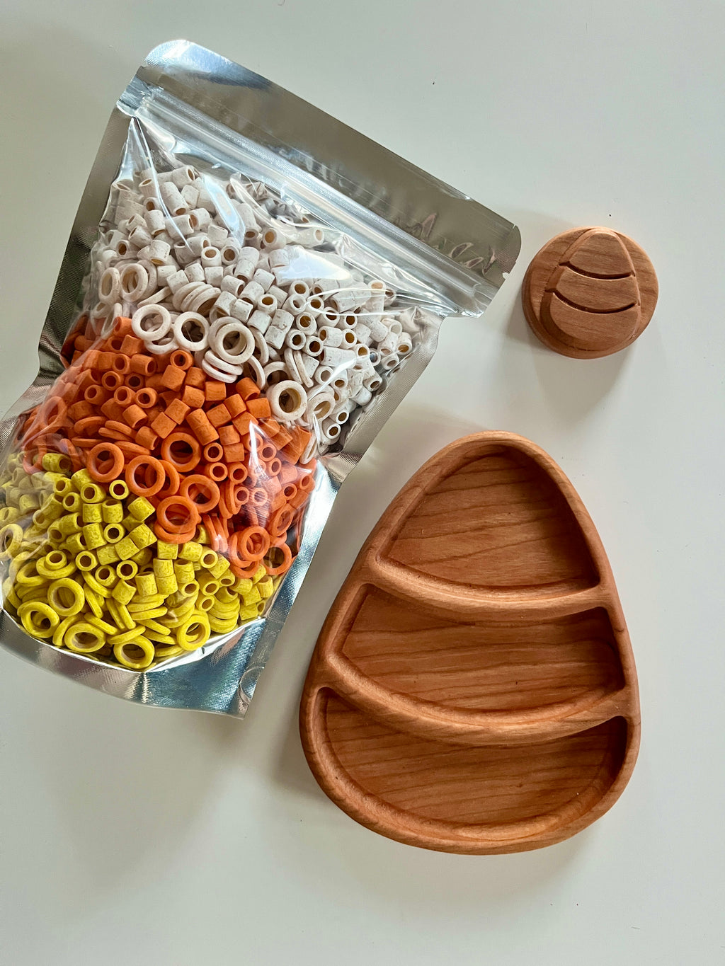 Clear resealable bag of small orange, yellow, and white pasta shapes next to a divided wood Easter egg tray and wooden candy piece
