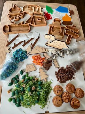 Wooden camping-themed shapes and tokens with colorful plastic rings, pasta, pebbles, and shredded natural materials on white surface