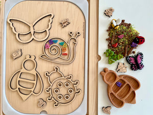 Wooden puzzle board with insect-shaped cutouts and colorful small bugs, next to a tray with dried moss and wooden insect figures