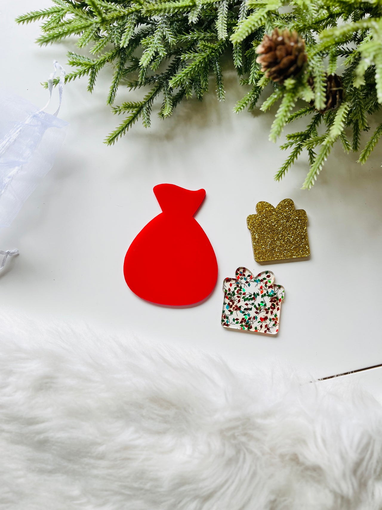 Red flat Santa sack cutout alongside two gift-shaped tokens, one gold glitter and one with red and green festive confetti, on white surface