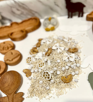 Close-up of sensory play materials including white shredded paper, white speckled balls, and small wooden shapes on a white surface