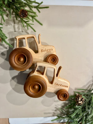 Natural wooden toy tractors with large engraved names Briggs and Stetson on plain background with pine branches and cones