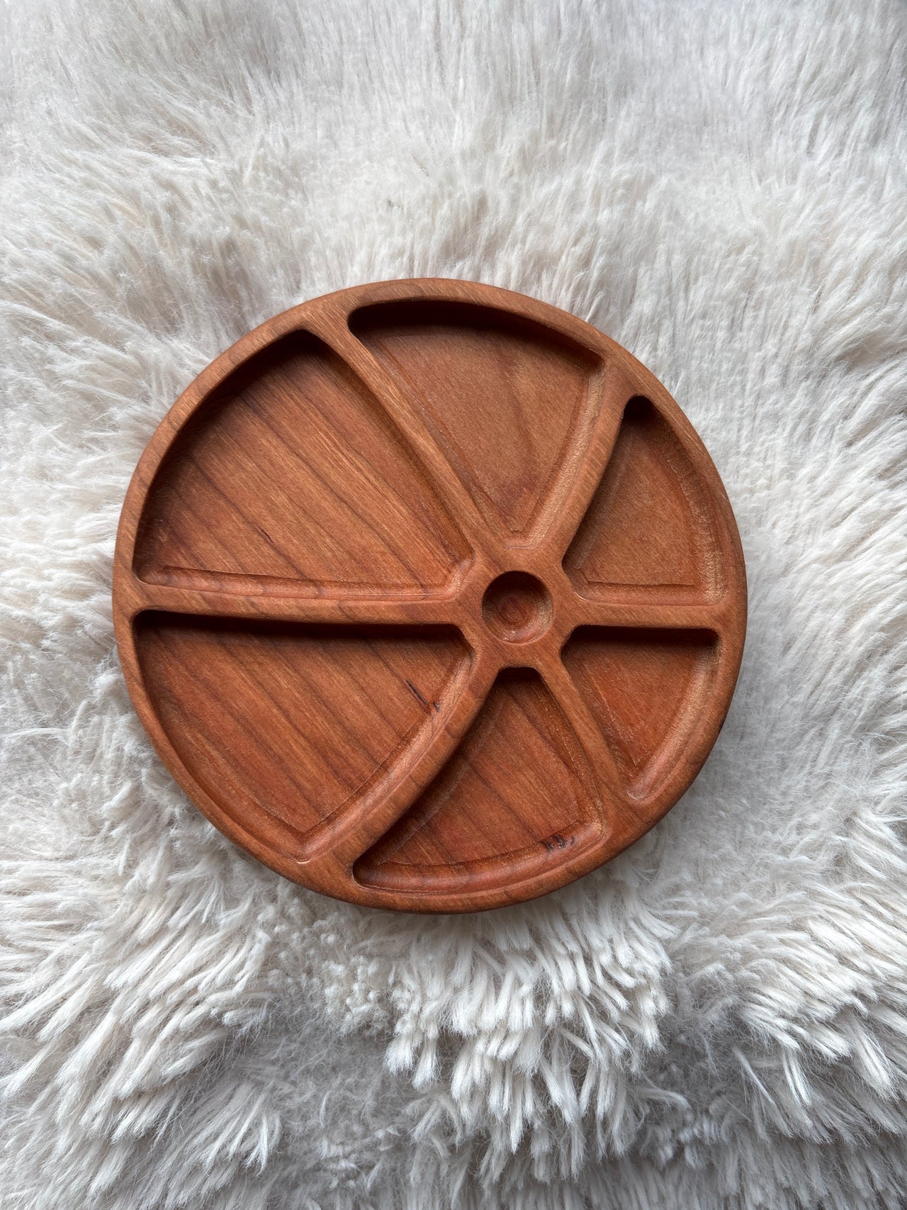 Round wooden tray with five curved compartments on a textured white fur surface