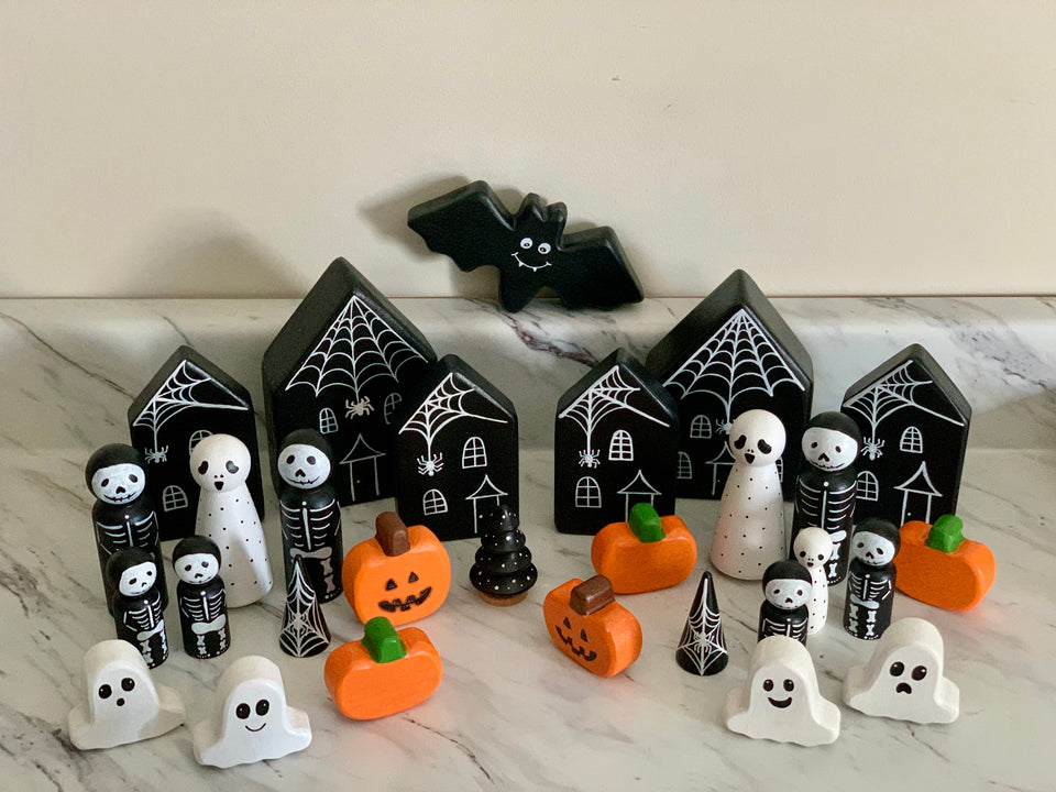 Wooden Halloween peg dolls with ghosts, skeletons, pumpkins, black haunted houses, spider webs, and a flying bat on marble surface