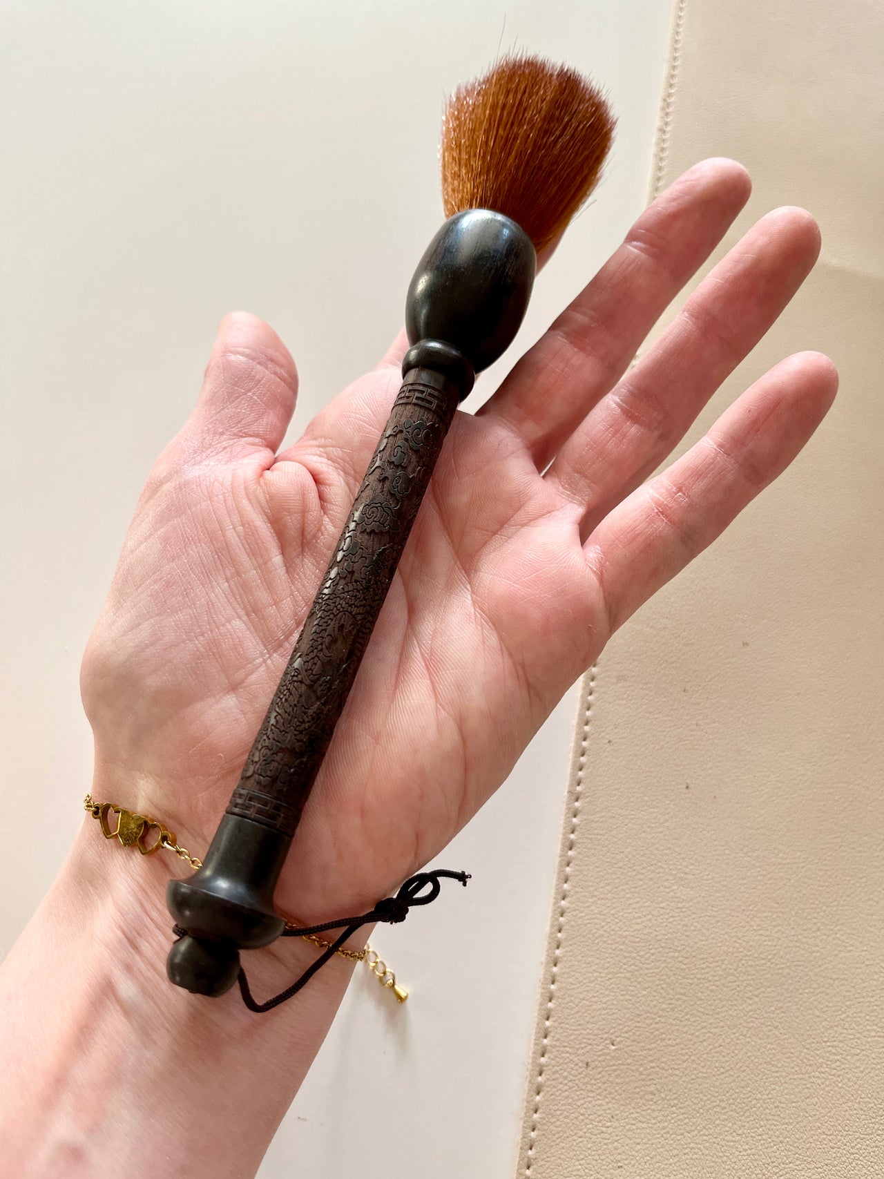 Hand holding a vintage-style makeup brush with an ornate dark wooden handle and soft brown bristles