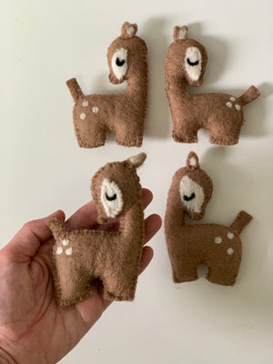 Handmade felt deer with closed eyes and white spots, displayed on white background with one held in hand