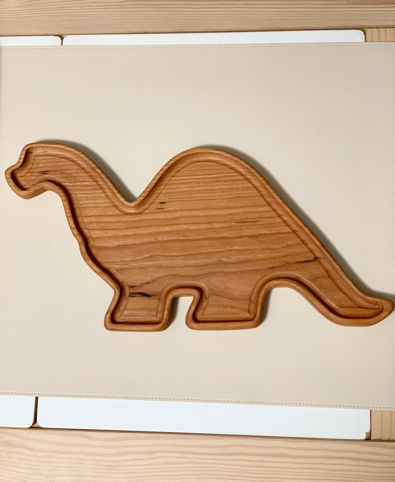 Wooden sensory tray shaped like a Brachiosaurus dinosaur with smooth carved edges on light surface