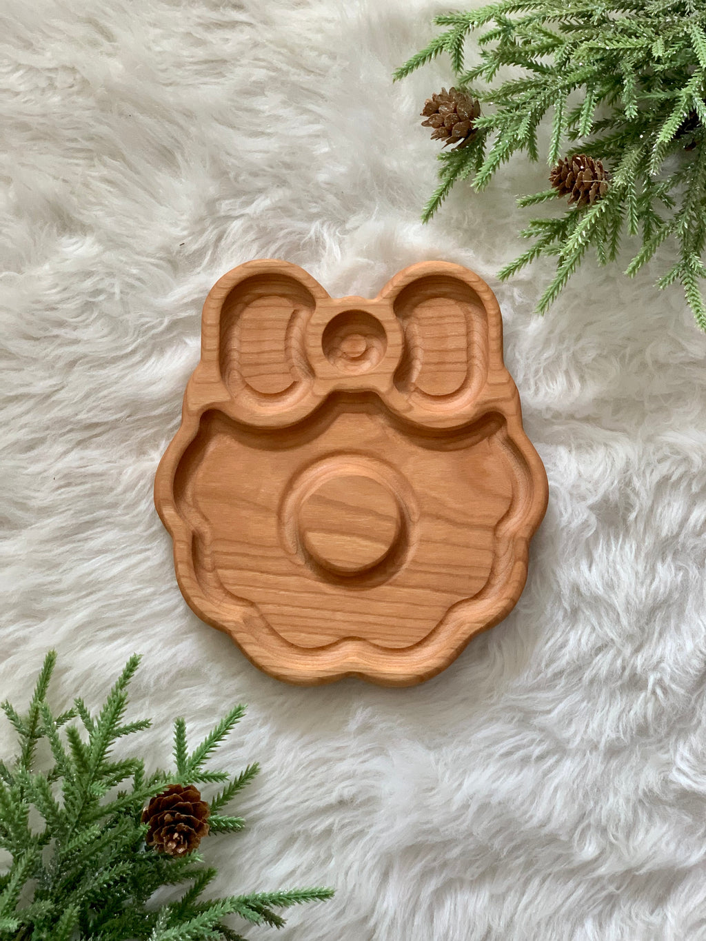 Wooden wreath-shaped sensory tray with bow detail placed on fluffy white surface with pine branches and pinecones nearby