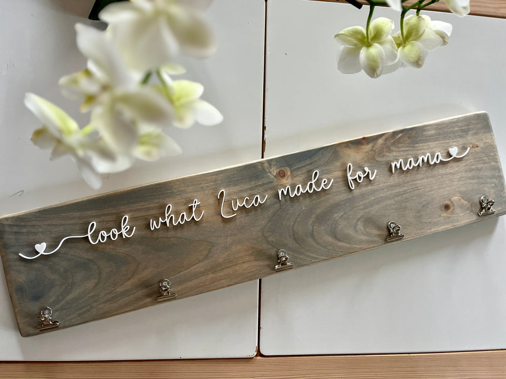 Custom wooden wall sign with white cursive letters reading "look what Luca made for mama" and metal hooks on stained wood