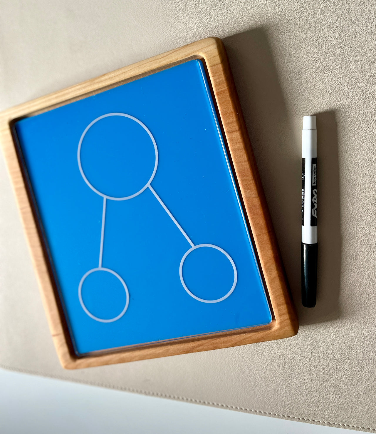 Wooden framed blue drawing board with three connected circles and black and white marker on beige surface