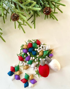 Assorted colorful fabric bulbs and white berries arranged on a white surface with pine branches and cones above