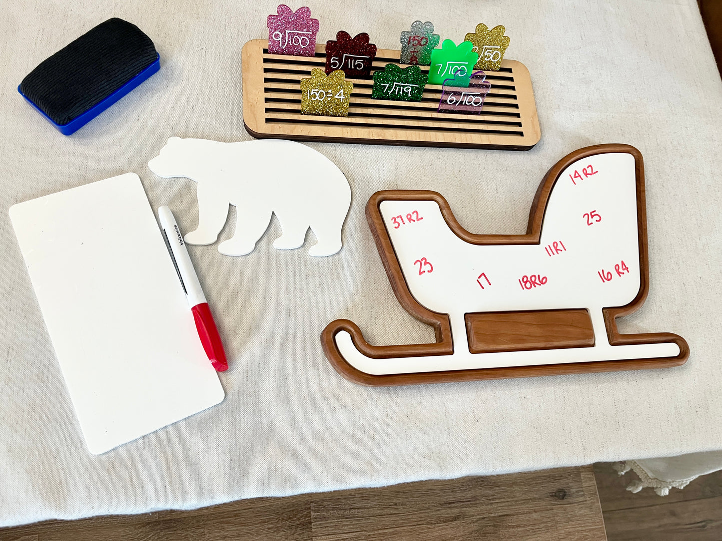 Wooden sled-shaped sensory tray with red markers, whiteboard, bear cutout, and wooden math flash cards on fabric surface