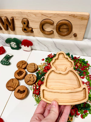 Hand holding a wooden tray shaped like a winter hat with wooden discs featuring winter icons on a festive background