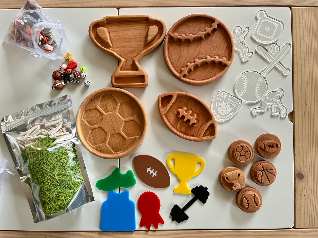 Wooden sports-themed trays and stamps with colorful sport-shaped cutouts and craft grass on a wooden table